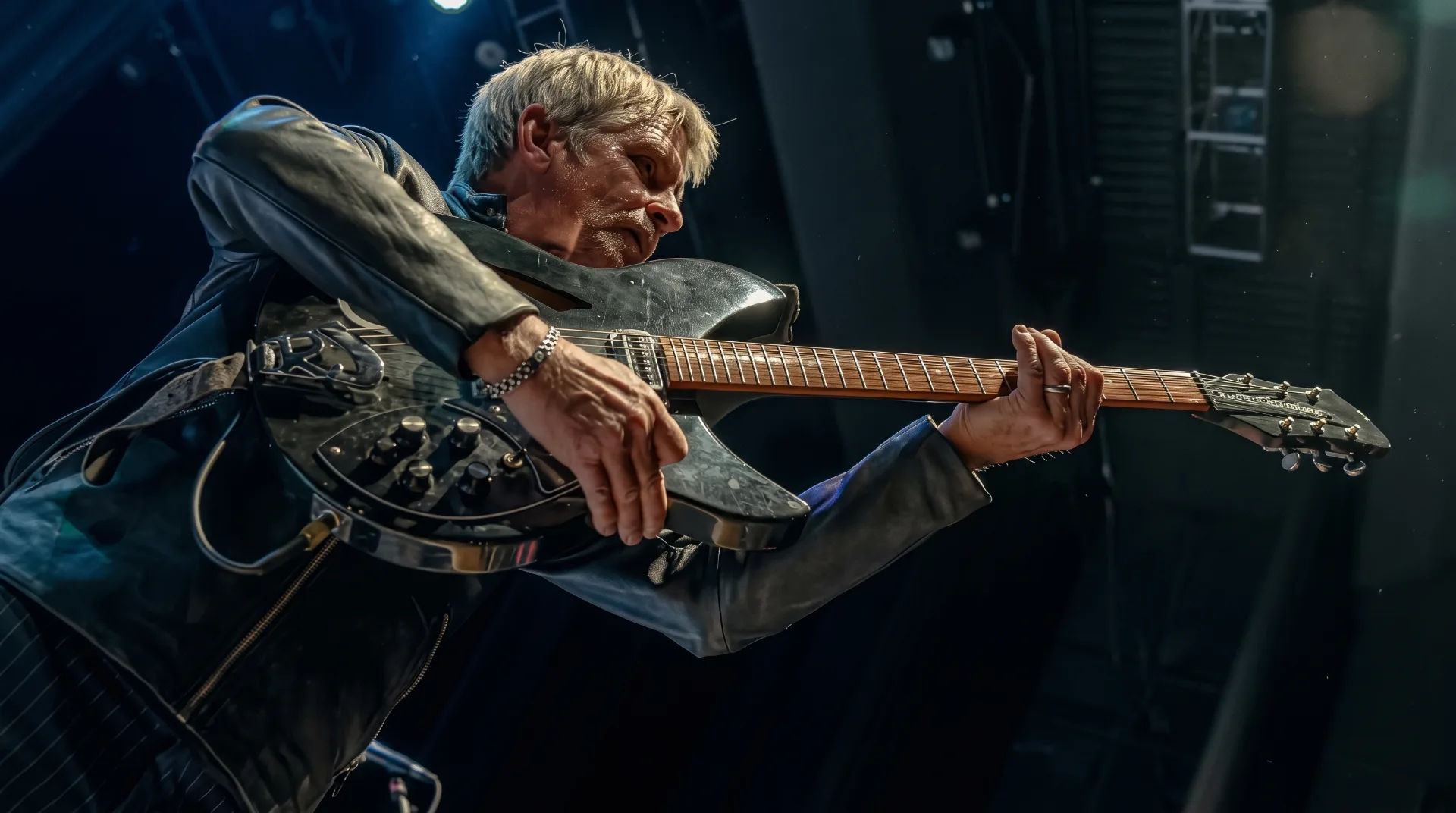 A musician passionately playing a guitar on stage, dressed in a leather jacket with dramatic lighting