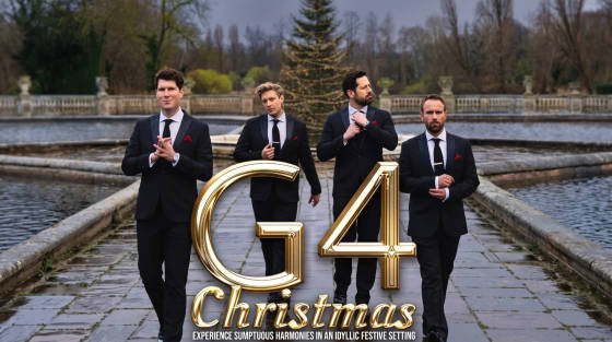 Four men in black suits walking by a water feature with a Christmas tree in the background
