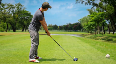 Golfer in grey shirt and cap ready to swing a driver on a golf course