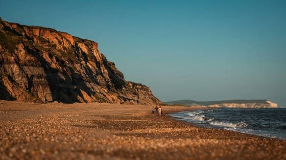 Rocky cliffs beside a pebbled beach with people walking