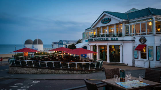 Exterior of Mr Rocks Cocktail Bar with red umbrellas and sea view