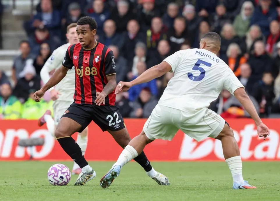 Bournemouth player in red and black kit dribbles past opponent in white kit during a match.