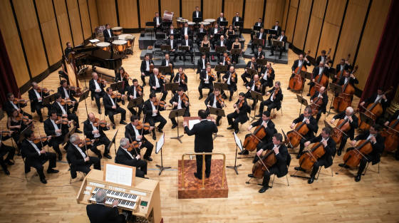 An orchestra performing with a conductor in front of musicians