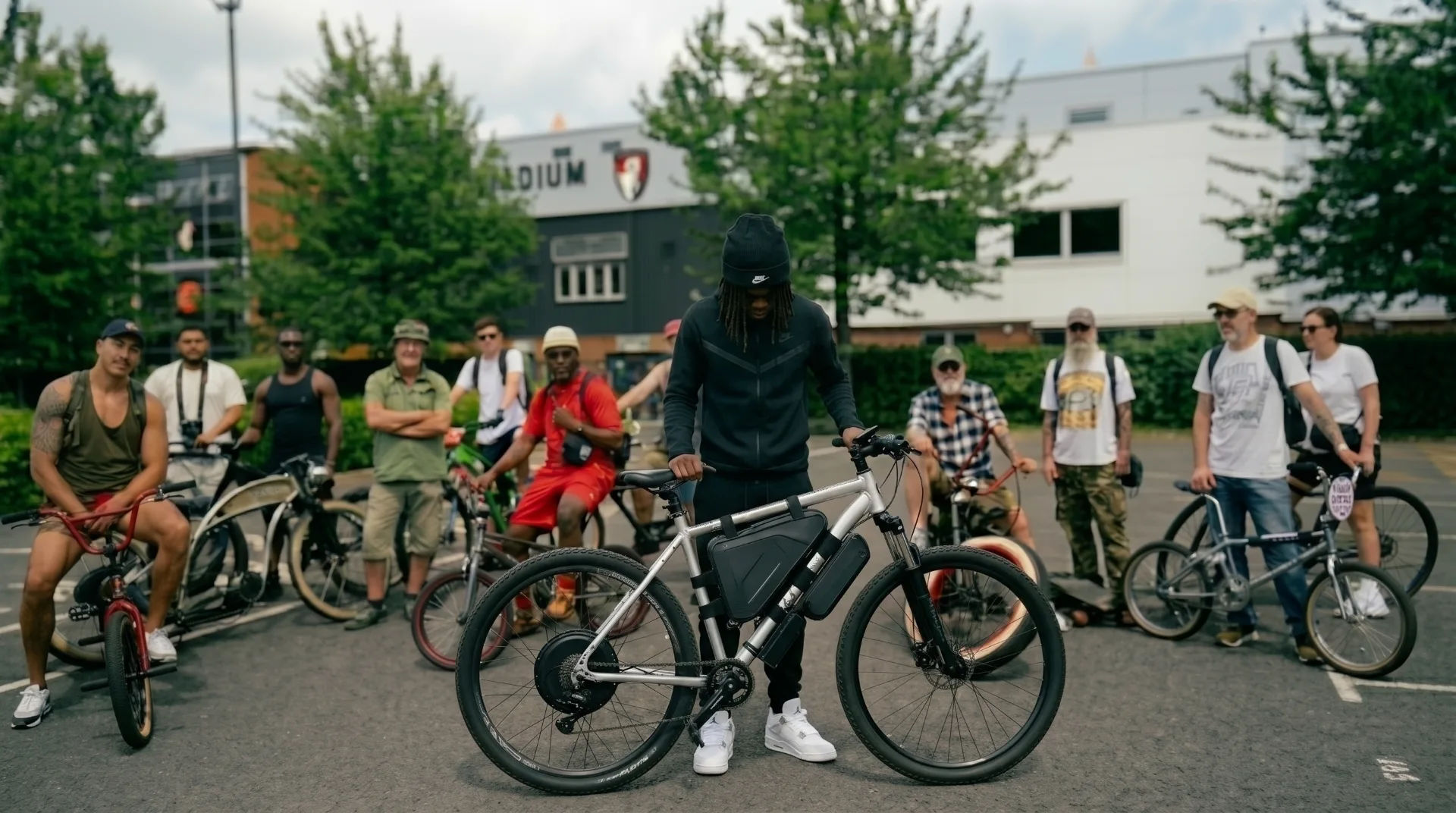 A group of cyclists gathered outdoors, with one person inspecting a bike in the foreground.