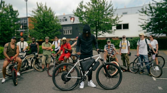 A group of cyclists with various bikes in front of a stadium