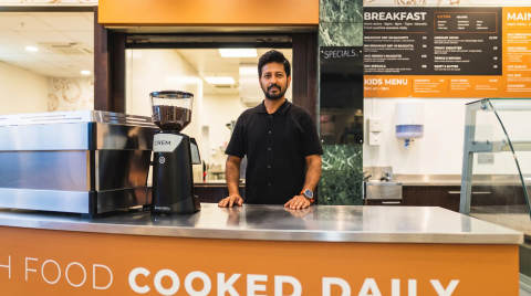 Barista standing at a cafe counter with a coffee grinder and menu