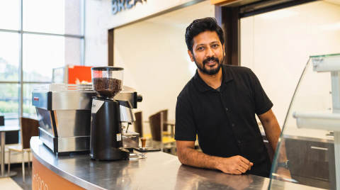 Barista leaning on a counter with coffee grinder and espresso machine