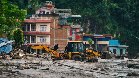 Workers operating a JCB backhoe loader in a muddy area near buildings