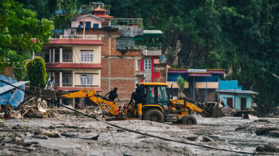Workers operating a JCB backhoe loader in a muddy area near buildings