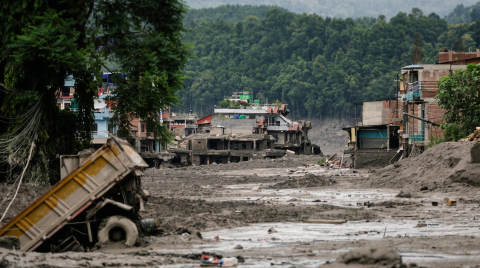 Abandoned buildings and a truck in a muddy area with trees in the background