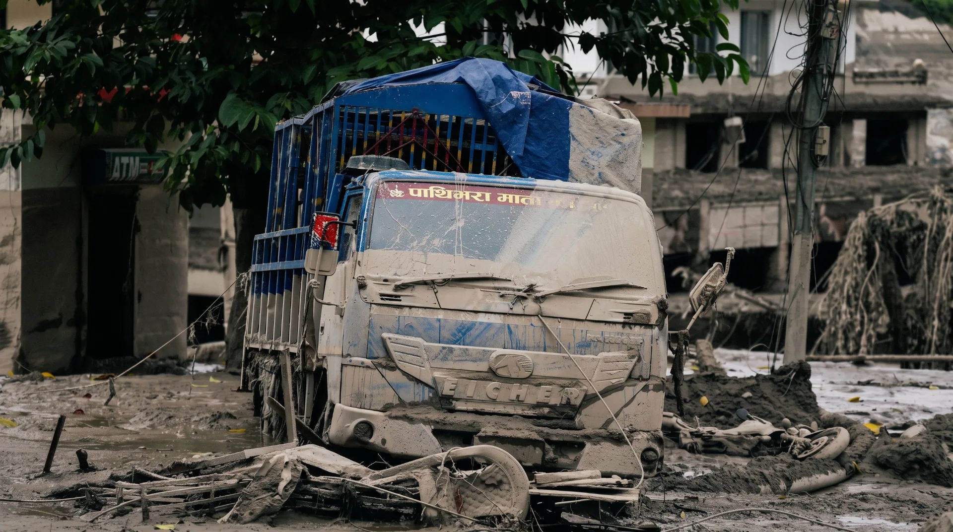 A damaged truck covered in mud and debris, surrounded by destruction from a flood disaster.