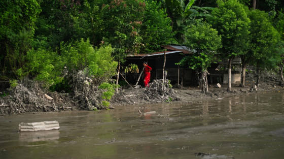 Woman in a red dress standing near a riverbank with lush vegetation
