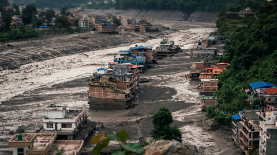 Houses on raised platforms along a dry riverbed with vegetation