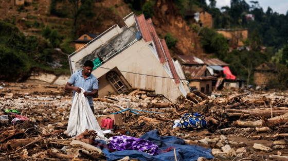 Man holding a blanket amidst debris and damaged buildings