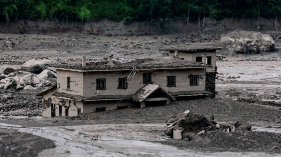A house partially buried in ash and debris with trees in the background