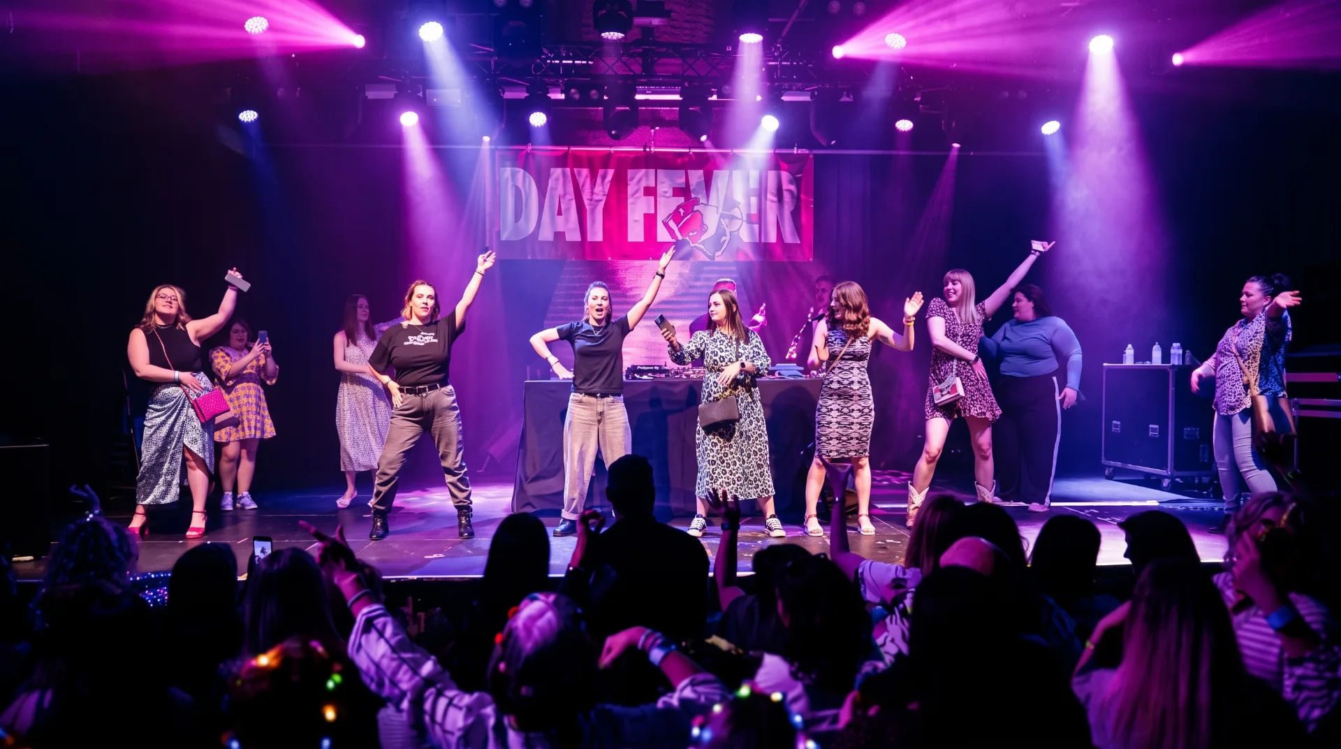 A lively performance on stage at O2 Academy with dancers and a DJ, illuminated by vibrant lights.