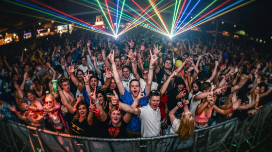 A large crowd at a music event with colourful laser lights