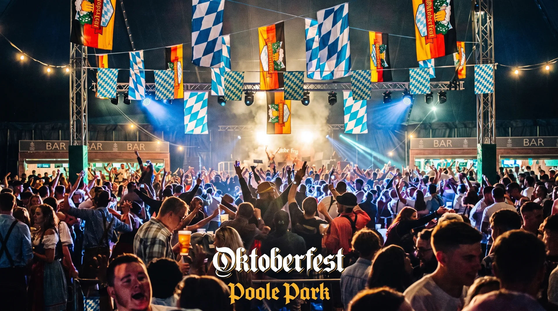 Crowd enjoying Oktoberfest in a large tent with flags, lights and a bar in the background