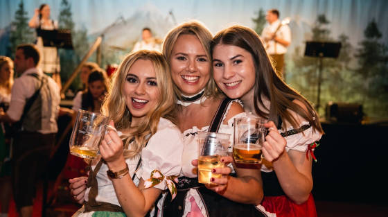 Three women in traditional costumes holding drinks at a celebration