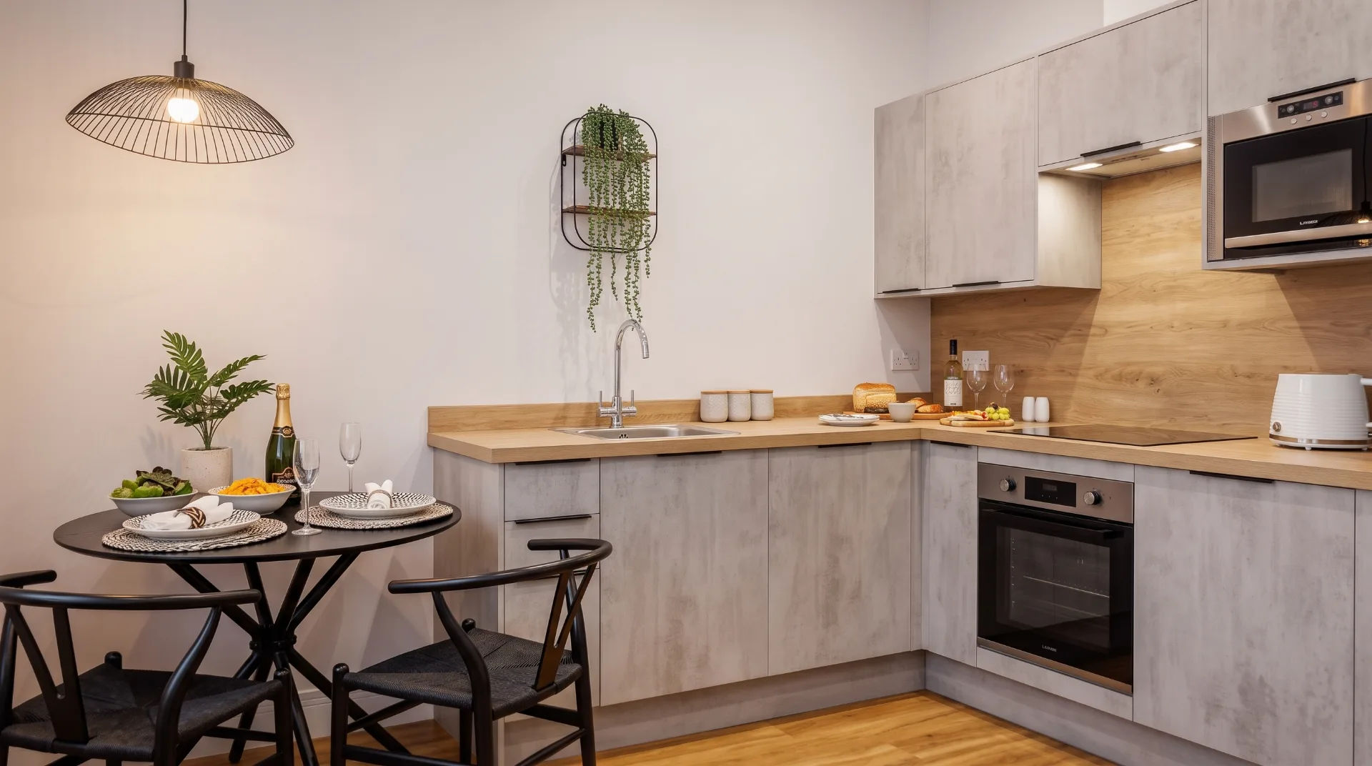 Modern kitchen with wooden accents, black round table set for dining, and champagne on the counter