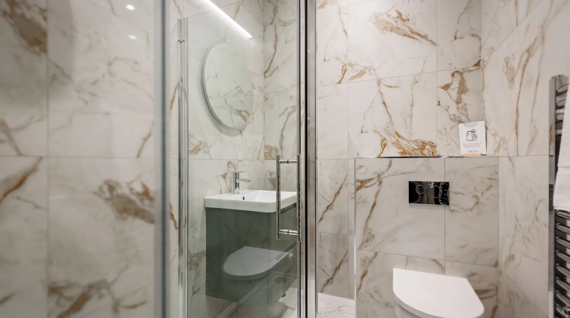 Modern bathroom featuring marble tiles, a glass shower, and a sleek sink with a round mirror