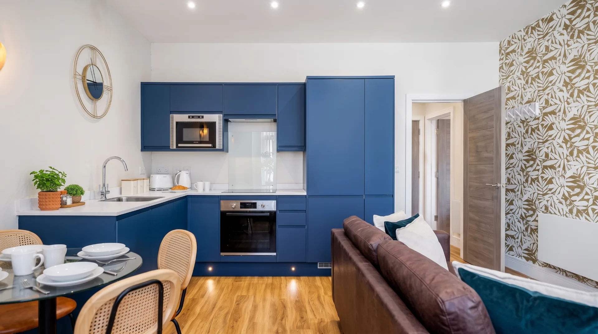 Modern kitchen and living area in Pebbles Apartments, featuring blue cabinets and a round dining table.