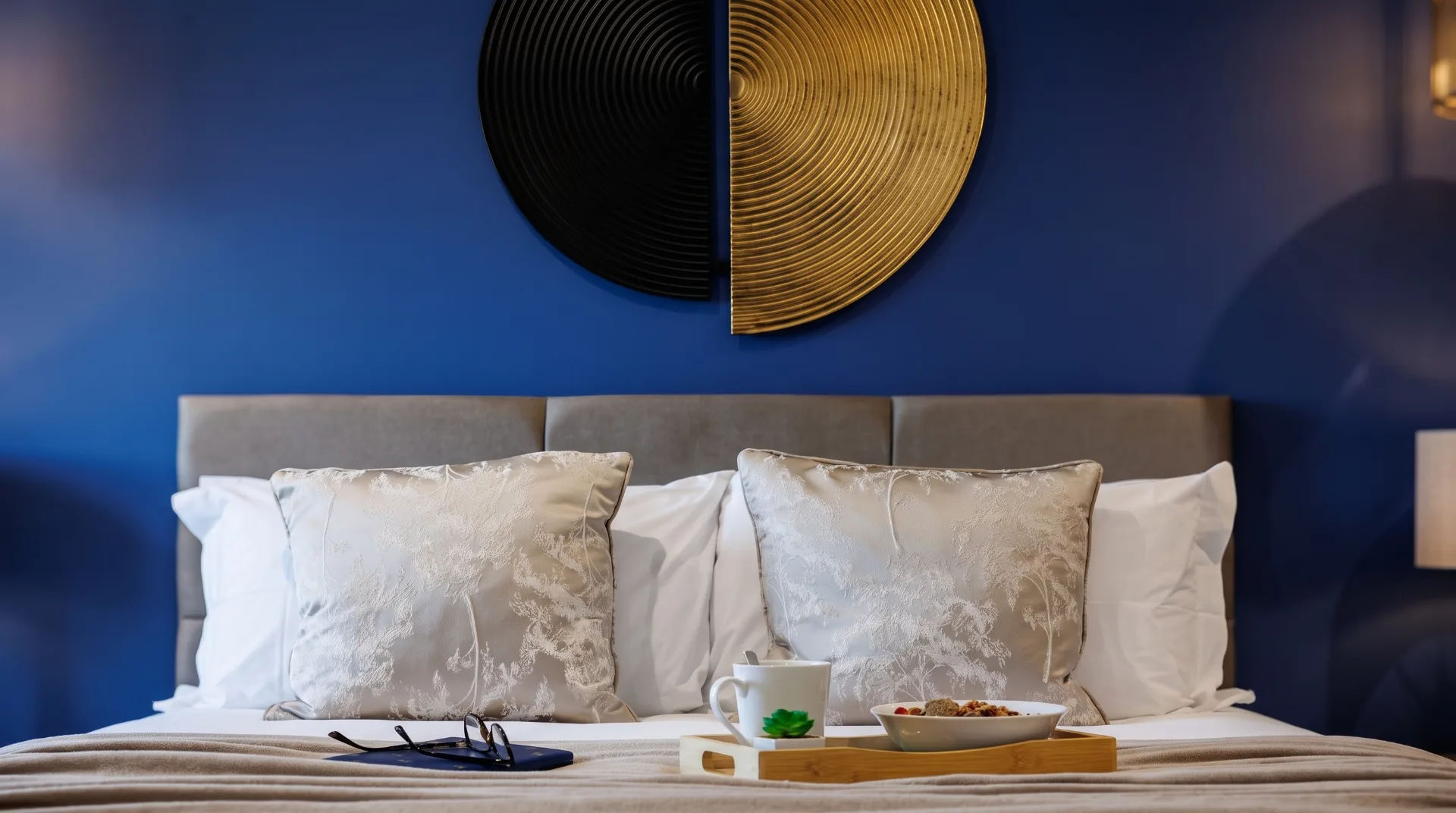 Stylish bedroom with blue wall, decorative pillows, a tray with breakfast, and glasses on the bed