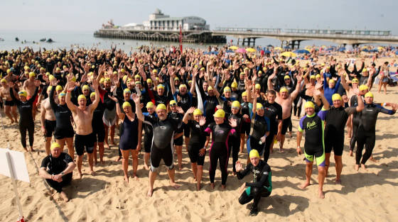 Many swimmers in wetsuits and yellow caps on Bournemouth beach