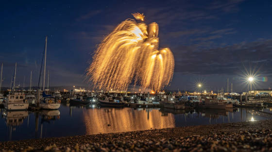 Fireworks illuminating the night sky above a marina with boats