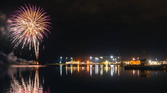 Colourful fireworks burst over a lit harbour at night