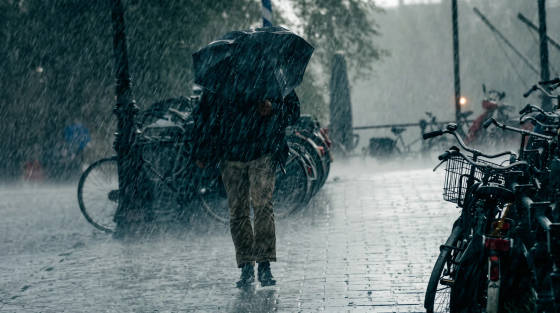 A person with an umbrella walking in heavy rain beside parked bicycles.