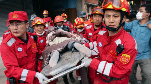 Rescue workers in red uniforms carry a person on a stretcher