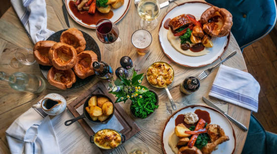 A table set with plates of roast dinner, Yorkshire puddings, and drinks