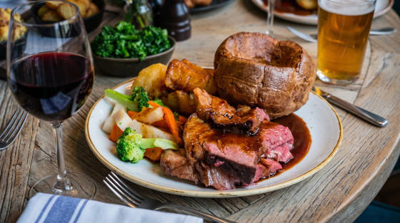 Plate of roast beef with Yorkshire pudding, vegetables, and a glass of red wine