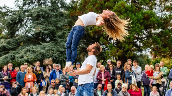 A man lifting a woman during an acrobatic performance in a park