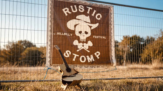 A guitar rests in front of a Rustic Stomp festival banner