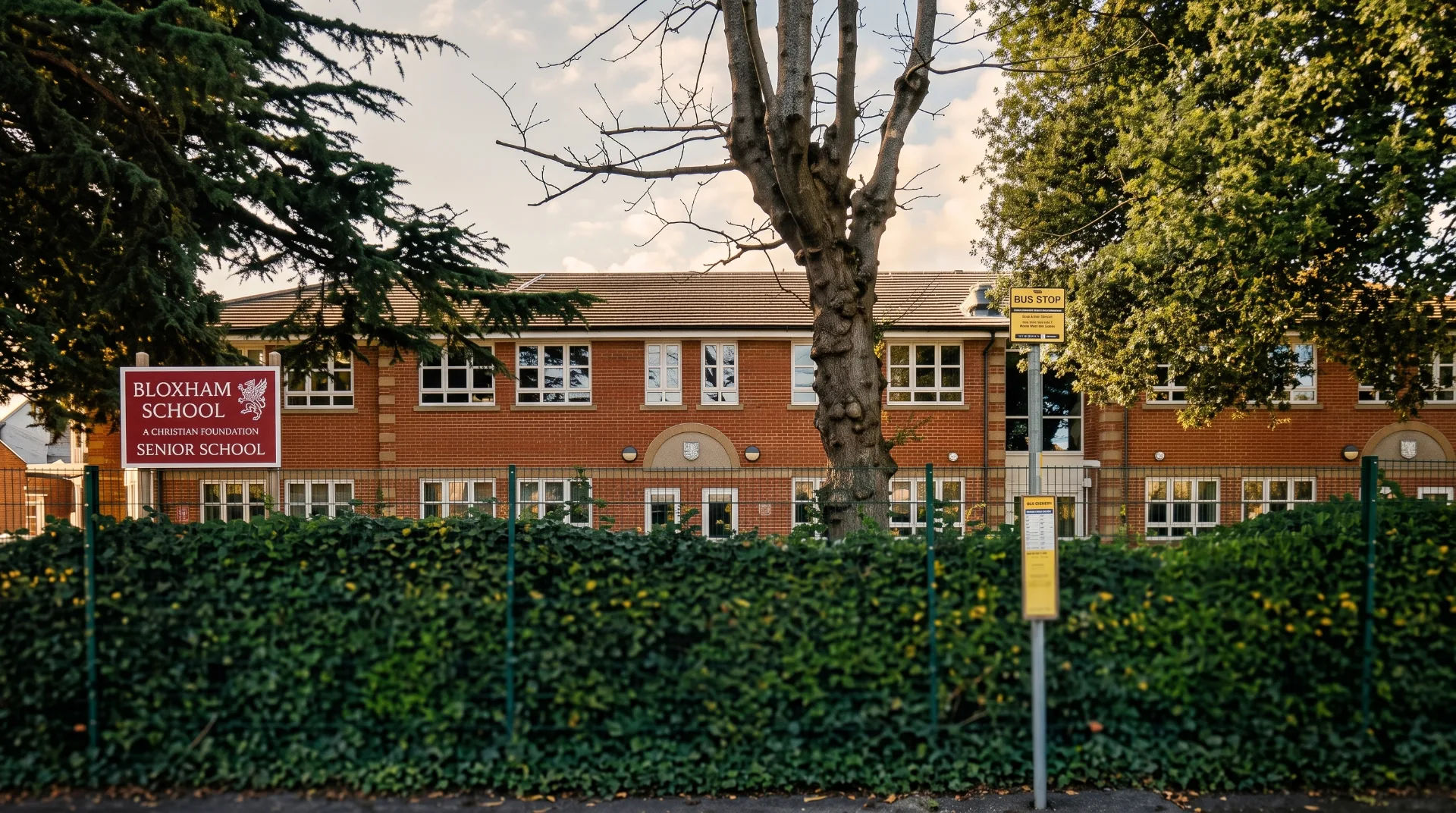 Bloxham School building with a sign, surrounded by greenery and a bus stop in front