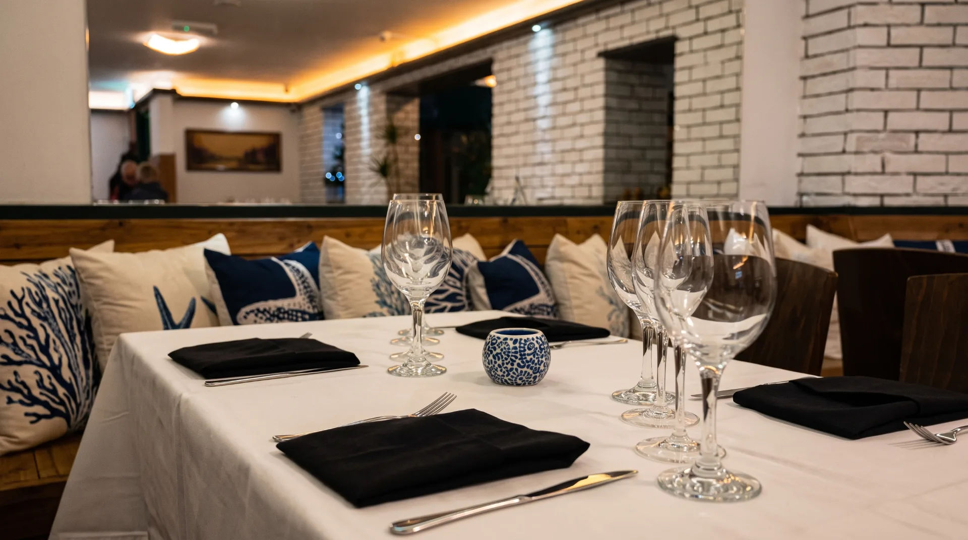 A dining table set with glasses, cutlery, and black napkins, surrounded by decorative pillows in a restaurant setting.