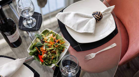 A dining table with a salad, wine bottle, glass, and cutlery