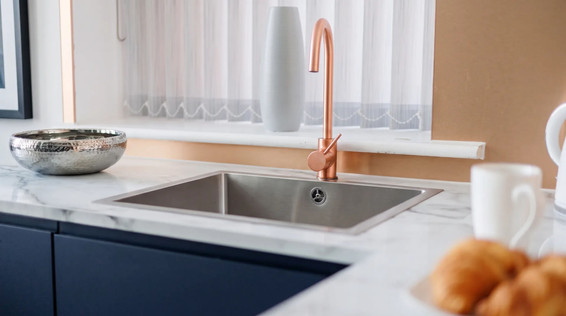 Modern kitchen sink with a copper tap, marble countertop, and a silver bowl