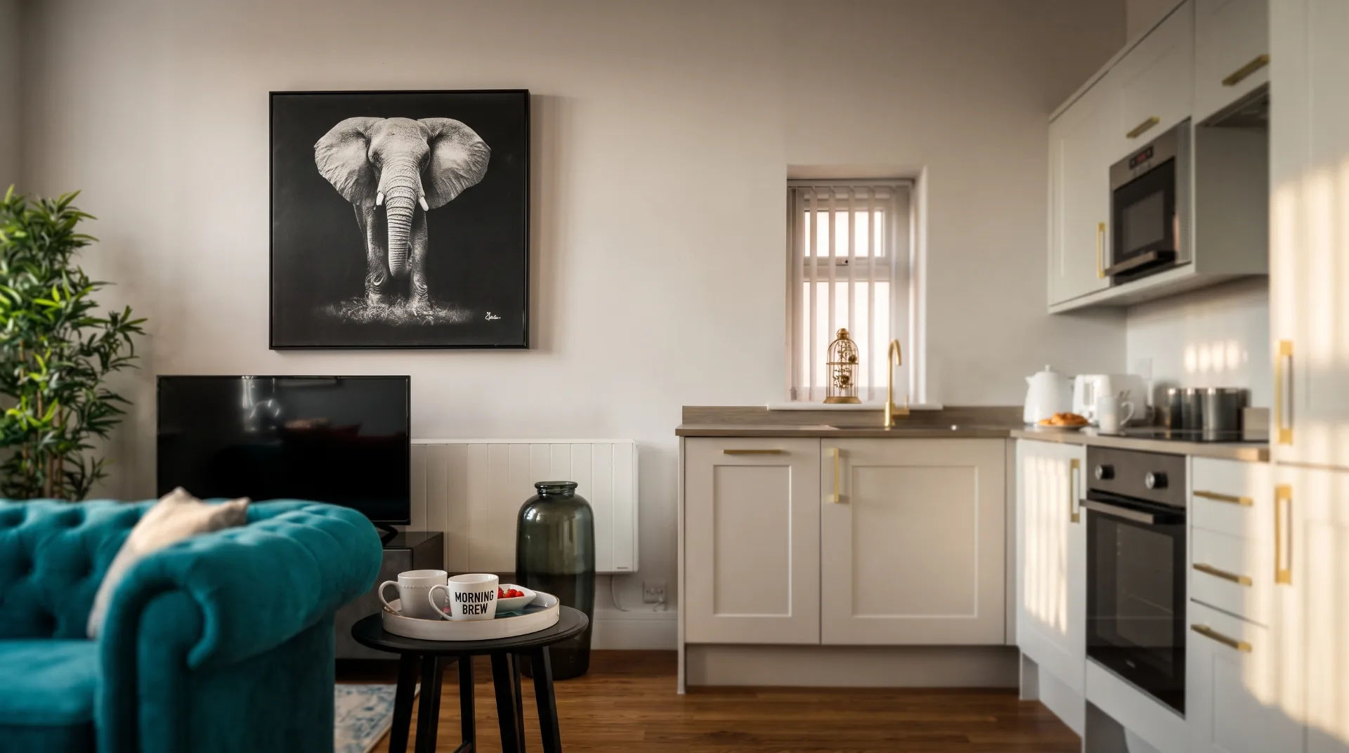 Stylish apartment interior featuring a teal sofa, modern kitchen, and elephant artwork on the wall