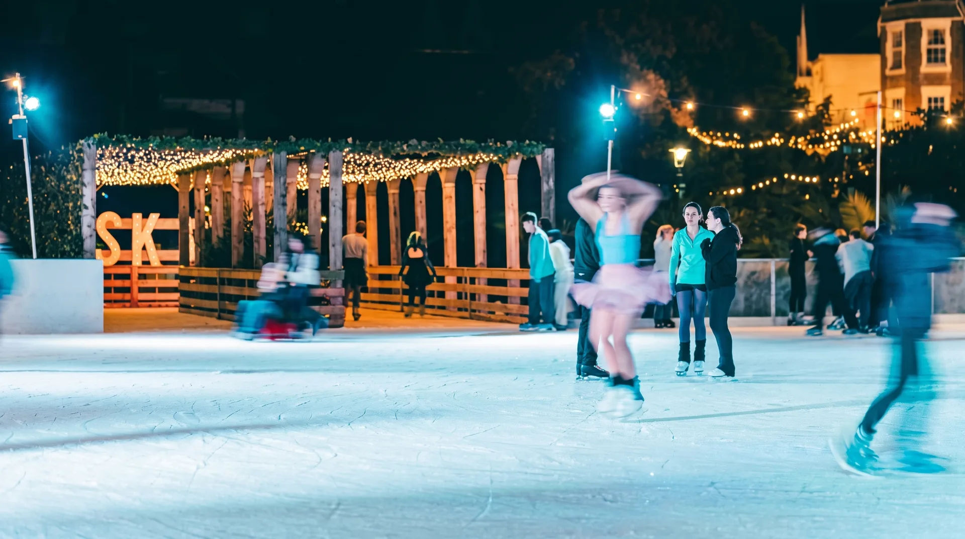 Skaters enjoying the open-air ice rink at night, with festive lights and a wooden structure in the background