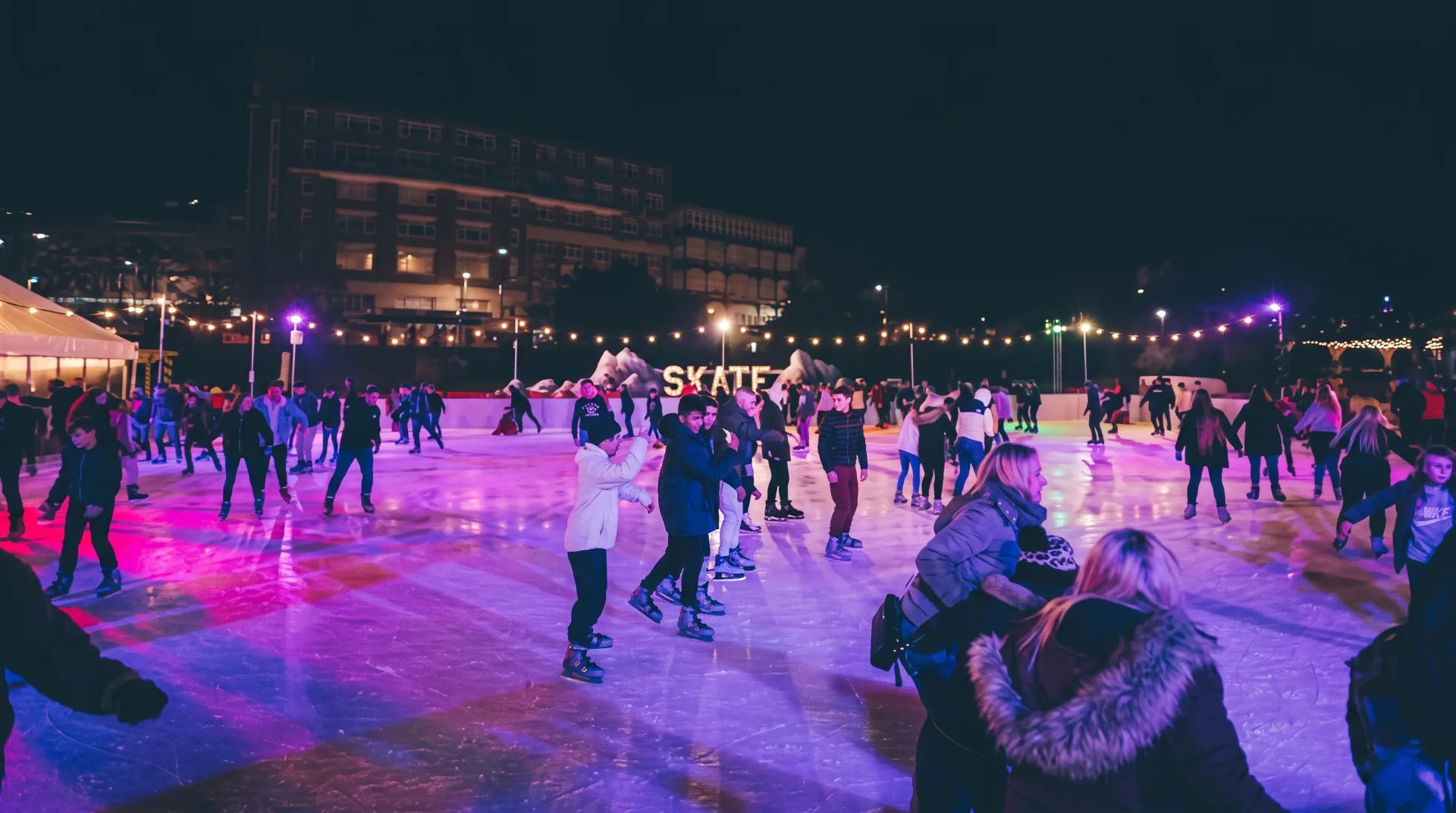 Skaters enjoying the open-air ice rink at night, illuminated with colourful lights in Lower Gardens, Bournemouth