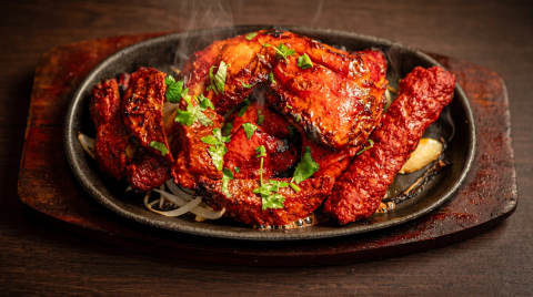Grilled chicken and sausages on a sizzling platter with herbs