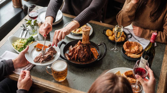 Table set with plates of food, drinks, and diners enjoying a meal