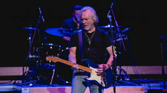 Musician playing electric guitar on stage with a drummer behind