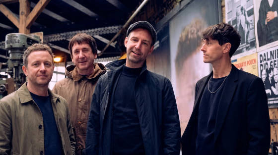 Four men standing together in an industrial space with posters behind them