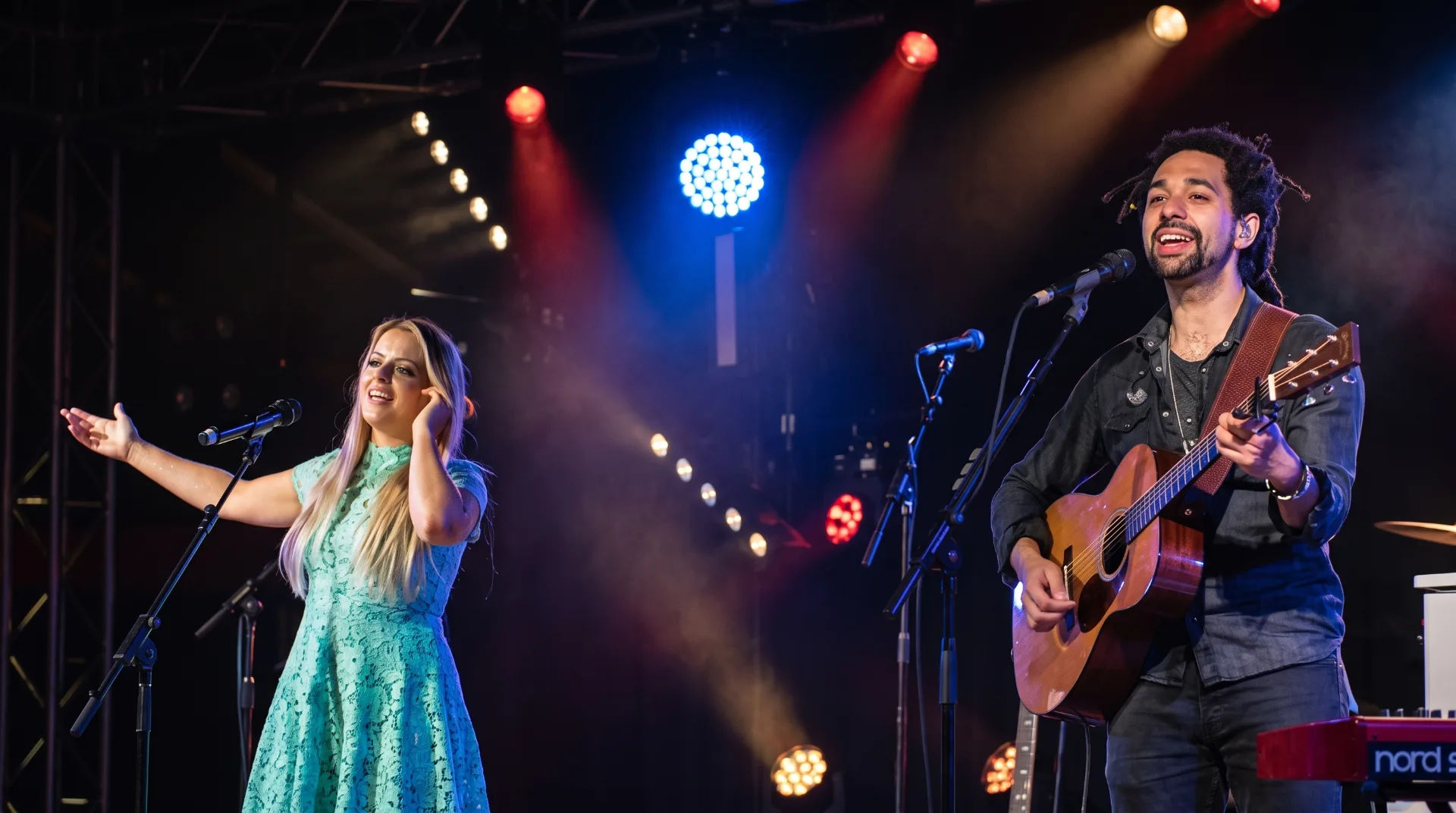 Two musicians perform on stage, one with a guitar and the other singing, under colourful stage lights.