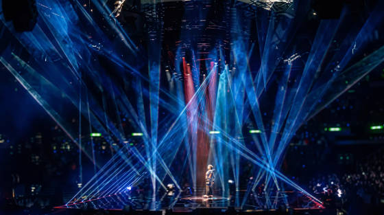 A performer on stage surrounded by vibrant laser lights