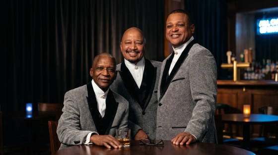 Three men in grey suits smiling at a bar